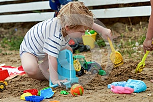 Little boy plays in the sand with plastic toys