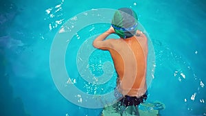 A little boy in the pool learning to swim, top view, he jumps into the water.