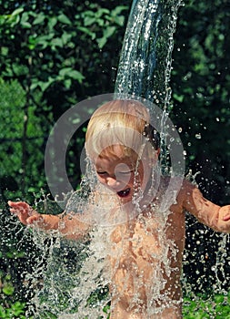 Little boy is poured with cold water from bucket. Kids water games on hot day in backyard. Hardening for health. Strengthen your