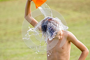 Little boy pouring cold water on his head outdoors