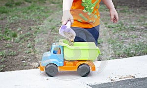 little boy pours sand into toy truck body, future builder