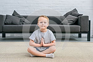 Little boy practicing yoga in lotus position in living