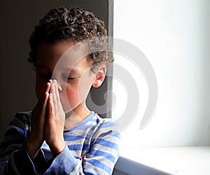 Little boy praying to God with hands held together stock photo