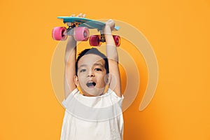 a little boy of preschool age is standing on an orange background in a white T-shirt, smiling fervently holding a skate