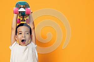 a little boy of preschool age is standing on an orange background in a white T-shirt, smiling fervently holding a skate