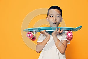 a little boy of preschool age stands on an orange background in a white T-shirt, smiling fervently holding his skate in