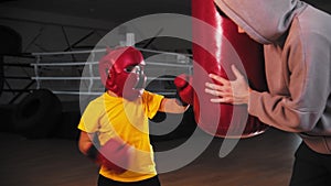 Little boy in protective helmet hitting the punching bag while the coach holding it
