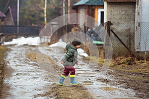 Little boy in protective rubber boots and rain clothes jumping in mud puddle. Happy child having fun while playing in