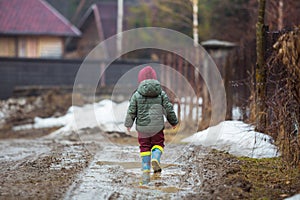 Little boy in protective rubber boots and rain clothes jumping in mud puddle. Happy child having fun while playing in