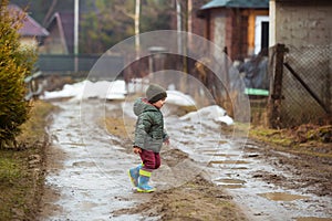 Little boy in protective rubber boots and rain clothes jumping in mud puddle. Happy child having fun while playing in