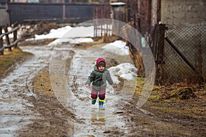 Little boy in protective rubber boots and rain clothes jumping in mud puddle. Happy child having fun while playing in