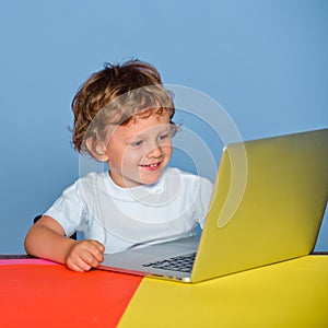 Little boy pupil with happy face expression near laptop, school concept. Kid with a notebook. Closeup portrait of clever