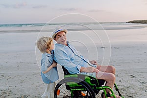 Little boy pushing his granfather on wheelchair, enjoying sea together.