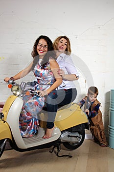 Little boy pushing a scooter with two girlfriends, studio photo