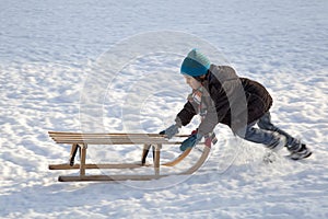 Little boy pushing sled uphills