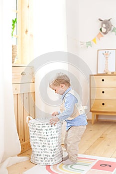 A little boy puts toys in a Scandinavian basket for a children`s room. Eco-friendly decor child`s room. Portrait of a boy playing