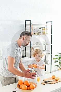 little boy putting orange in squeezer for making fresh juice while father helping him