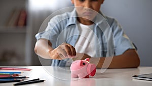 Little boy putting pocket money in piggy bank, raising funds for desired toy photo