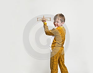 Little boy in pyjamas with wood toy plane. Yawning blond kid in pyjamas with dinosaur animals pattern and map print