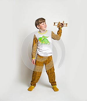 Little boy in pyjamas with wood toy plane. Yawning blond kid in pyjamas with dinosaur animals pattern and map print