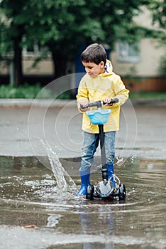 Little boy in raincoat and rubber boots playing in puddle. Fun on street.