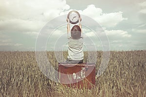 Little boy raises in the sky a watch in a surreal landscape