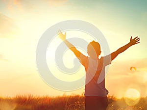 Little boy raising hands over sunset sky