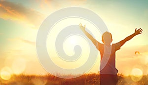 Little boy raising hands over sunset sky