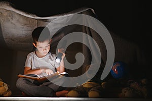 Little boy reading book in play tent at night