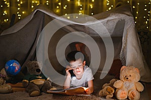 Little boy reading book in play tent at night