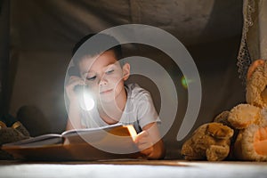 Little boy reading book in play tent at night