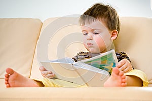 Little boy reading book on sofa