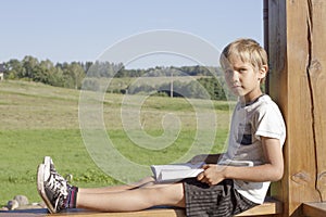 Little boy reading book at summer terrace. Casual clothes. Nature background. People, education, knowledge concept