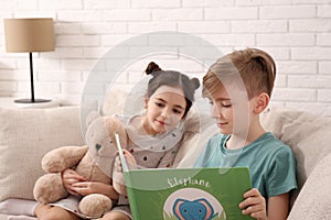 Little boy reading book to girl with toy bear on sofa