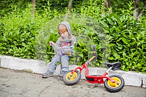 Little boy reading a book under big linden tree