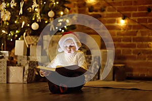 Little boy reading a magic book in decorated cozy living room. Portrait of happy kid on Christmas eve