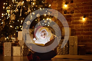 Little boy reading a magic book in decorated cozy living room. Portrait of happy kid on Christmas eve