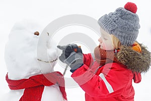 Little boy in red clothes having fun with big snowman. Active winter outdoor leisure for children. Child during stroll in a snowy