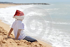 Little boy in red Santa hat looking at ocean waves