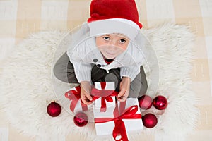 Little boy in red santa hat with many gift boxes with red ribbon and christmas ball. Child with Christmas present, banner copy
