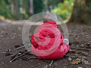Little boy in a red waterproof sits in a mandala on the floor in the woods