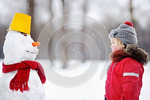 Little boy in red winter clothes having fun with snowman