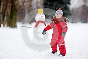 Little boy in red winter clothes having fun with snowman