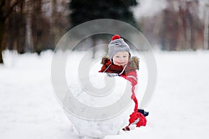 Little boy in red winter clothes having fun with snowman