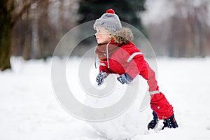 Little boy in red winter clothes having fun with snowman