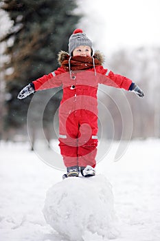 Little boy in red winter clothes having fun with snowman