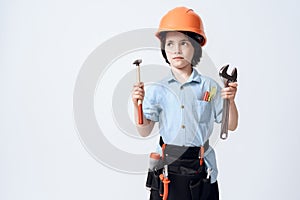 A little boy in repairman form and helmet. Boy holds a adjustable spanner and hammer in his hand.