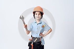 A little boy in repairman form and helmet. Boy holds a adjustable spanner in his hand.