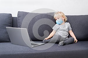 A little boy in a respiratory mask stays home in quarantine and watches cartoons on a laptop