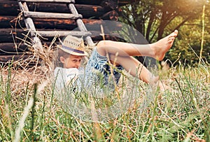 Little boy rest in green grass near the hayloft in garden